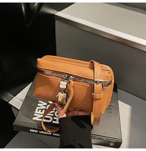 Detail of tan leather crossbody bag featuring a robot metal charm and adjustable strap