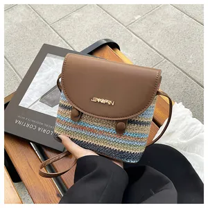 Detail of colorful woven straw bucket bag with brown leather flap and gold metal logo
