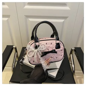 Close-up of pink pleated handbag with black bow prints and a pearl lace charm detail