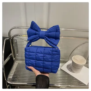 Close-up of royal blue quilted handbag with a large puff bow detail on metal shelf
