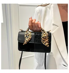 Detail of a black square crossbody bag with leopard print accent and yellow scarf detail