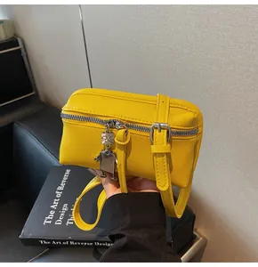 Detail of yellow pebbled leather crossbody bag featuring a silver robot charm and zipper