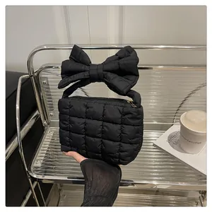 Detail view of black quilted puffer handbag featuring a bold oversized bow on the handle
