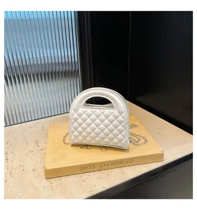 Detail of white quilted crossbody bag with top handle on a yellow art book stand