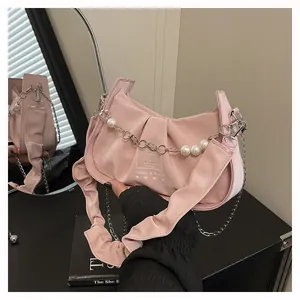 Pink velvet hobo bag featuring pearl chain details and decorative text on black surface