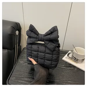 Close-up of a black quilted puffer handbag with a large bow detail and textured finish