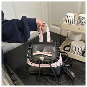 Detail eines Mini-Rucksacks in Schwarz und Rosa mit Spitze und Herzanhänger in der Hand