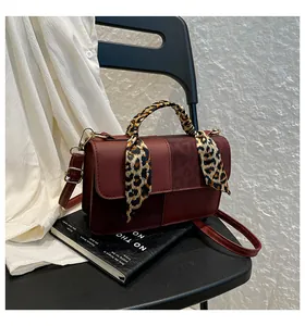 Close-up of burgundy leather crossbody bag with leopard print scarf handle and metal strap buckle