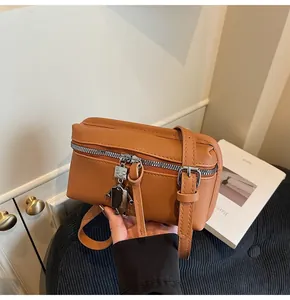 Close-up of caramel faux leather bag featuring a cute robot charm and silver zipper detail