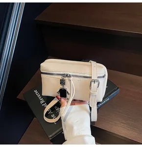 Detail of beige textured PU leather crossbody bag with unique metal robot charm and zip closure