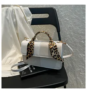 Close-up of cream crossbody bag with leopard print scarf handle and cross-stitch detail