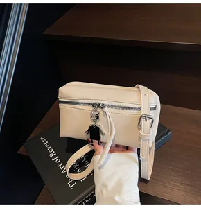 Detail of off-white mini crossbody bag with a robot charm and silver zipper texture