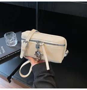 Detail of cream square shoulder bag featuring silver robot charm and tassel zipper