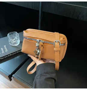 Detail of a brown leather square bag with a silver robot charm and adjustable strap