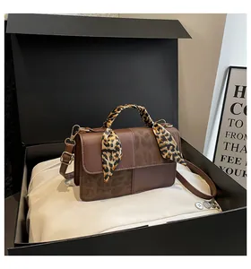Detailed view of a brown leopard print crossbody bag with silk scarf on a black gift box