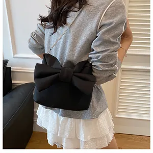 Detail of the black fabric bag with a large bow and silver chain on a model