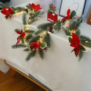 Close-up of frosted pine needles with red poinsettia and warm LED lights on white table