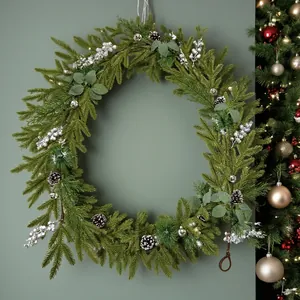 Detail view of a Christmas wreath with pine needles, cones, and silver berries on a green wall