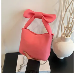 Detail of bright pink handbag featuring a large bow handle and elegant metal chain strap