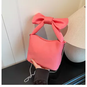 Detail of a bright pink canvas bag featuring a large bow handle and silver chain strap