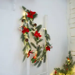 Christmas garland with red poinsettia, pine needles, cones and LED lights on a white ladder