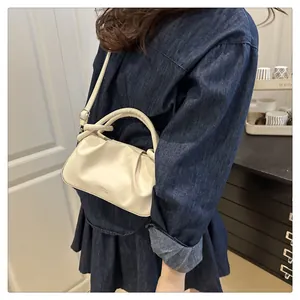 Détail du sac plissé en cuir crème avec lettrage doré et bandoulière de précision