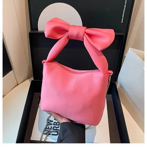 Detail of hot pink satin bag featuring a large bow handle and thin metal chain strap