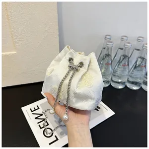 Détail de la broderie florale sur sac seau en dentelle crème avec chaîne et perle