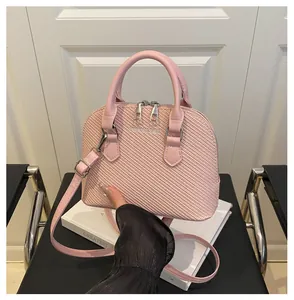 Detailed close-up of pink woven shell bag featuring metal fashion logo and silver hardware