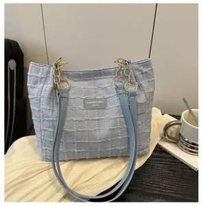 Detail of light blue waffle-textured tote bag with gold chain and leather straps