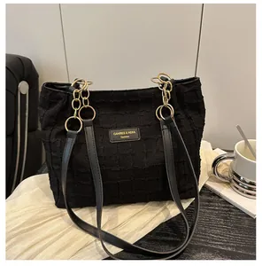 Detail of black textured tote bag with golden chain strap and brand logo plaque