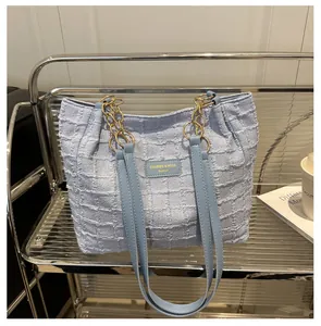 Detailed close-up of light blue textured tote bag with chain strap on metal rack