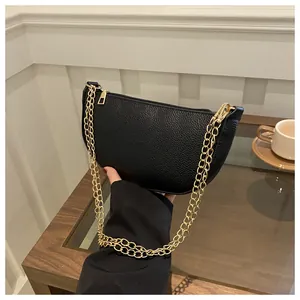 Detail der schwarzen Baguette-Tasche aus genarbtem Leder mit glänzenden Goldketten