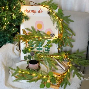 Close-up of lighted Christmas garland with pine needles, cones, and gold ornaments