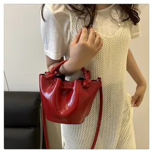 Detailed view of red glossy leather bucket bag with chunky knotted handle and logo