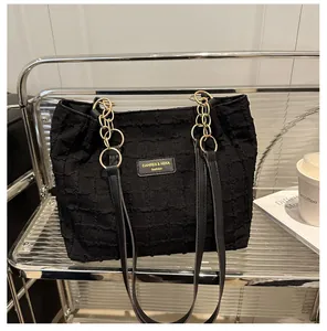 Detail of black textured tote bag featuring gold chain strap and stylish brand label