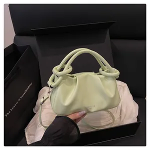 Détail du sac froissé vert clair avec logo argenté et poignée ronde sur fond de soie