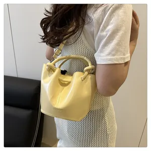 Detail of a creamy yellow glossy leather bucket bag with drawstring and logo