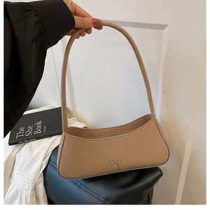 Detailansicht einer beige Baguette-Tasche mit goldener Metallschleife und Lederstruktur