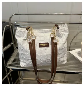 Detailed shot of white woven tote bag with brown leather tag and gold chain rings