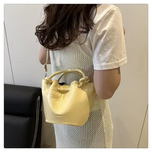 Model view of a pale yellow bucket bag with knotted handle and embossed fashion logo