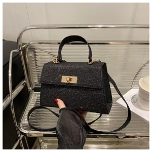 Detail of black glitter crossbody bag featuring golden twist lock and top handle