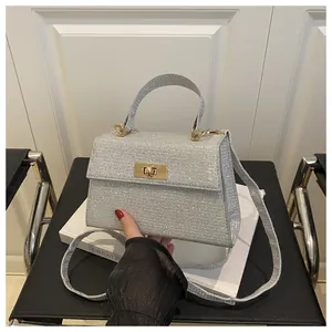 Detail of silver sequin handbag featuring a gold square twist lock and top handle strap