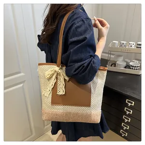 Detail of a large straw tote bag with brown leather handles and lace bow decoration