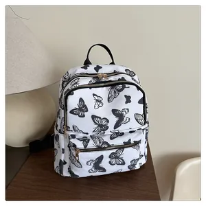 Detailed view of black butterfly print on white canvas backpack with gold hardware