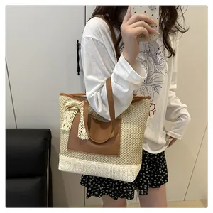 Close-up of woven straw tote bag with brown leather handles and lace bow detail