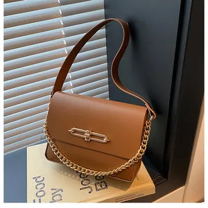 Close-up of caramel leather handbag featuring a sleek gold metal twist lock and chain strap