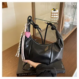 Detail of black crescent hobo bag with knotted strap and pink heart charm on books