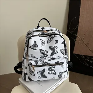 White canvas backpack with black butterfly prints and gold zipper details on a chair