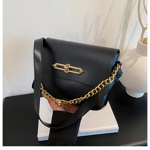 Detail of minimalist black handbag showing gold rectangular buckle and chunky chain strap